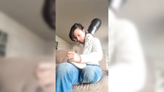 Asian student girl hugging huge black dildo on couch in sweater jeans