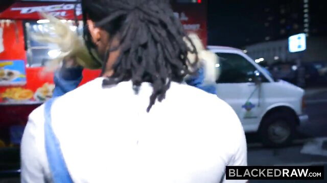 Blonde woman in white top hugs black guy with dreads at taco truck night