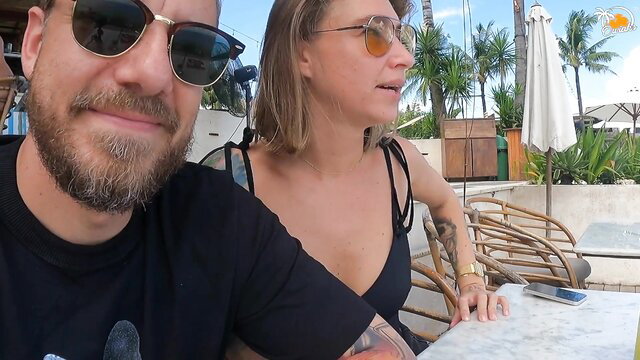 Tattooed blonde in black bikini with bearded guy smiling at beach resort