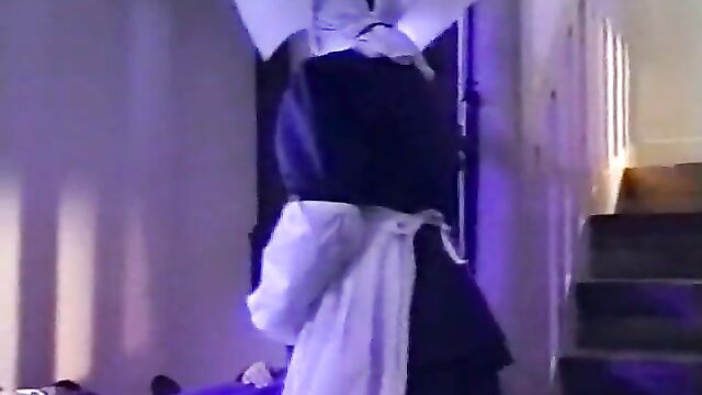 Nun in black habit and white apron bends over in dimly lit hallway