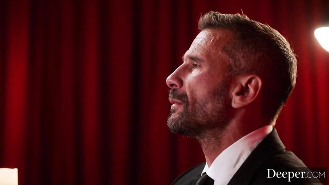 Manuel Ferrara profile in suit on red stage, Deeper adult video thumbnail