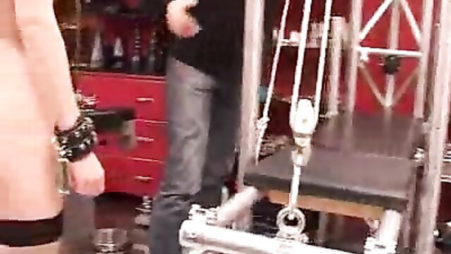 Busty blonde in black cuffs at BDSM sex swing setup