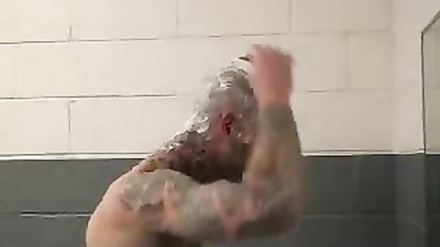 Tattooed muscular man getting headshave in restroom shower