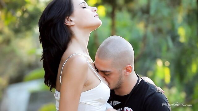Bald guy kissing stunning black-haired teen's breasts outdoors