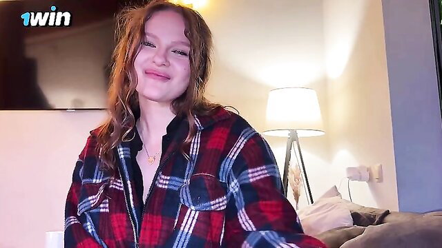 Smirking redhead teen in plaid shirt smiles seductively on couch