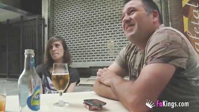 Young Spanish brunette with beer smiles at man at outdoor table