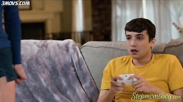 Stepmom in shorts stands over shocked gamer boy on couch