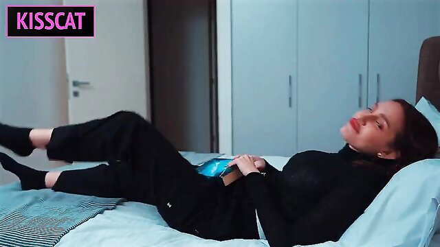 Hot brunette stepmom in black turtleneck and pants lying seductively on bed