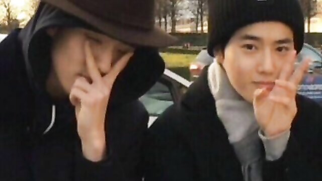 Two young Asian men making cute hand signs outdoors, hoodies and hats