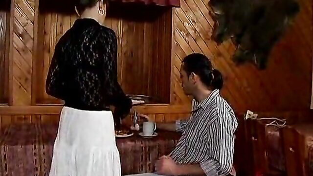 Mature 70yo Oma in lace top and skirt serves tea to man in wooden room