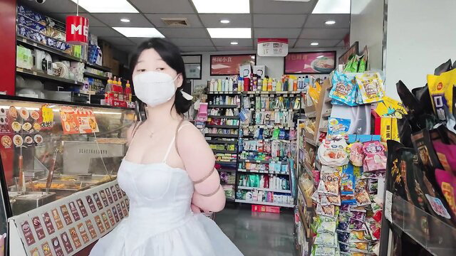 Chinese girl in white dress with bound arms in store exhibitionism