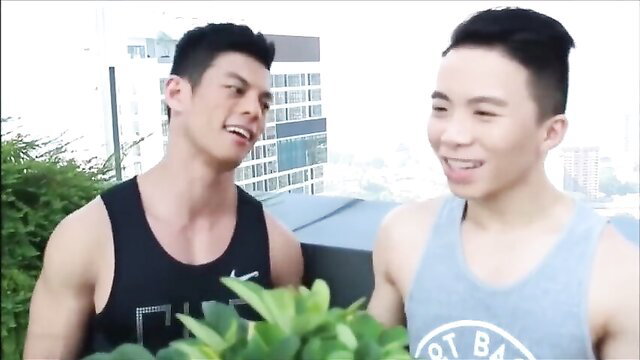 Two hot Asian twinks in tank tops smile outdoors on rooftop
