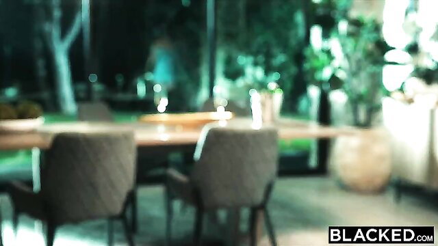 Blacked outdoor dining table scene with chairs, plants, wine glasses