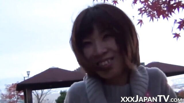 Smiling Asian woman with bangs in gray sweater, autumn outdoor park