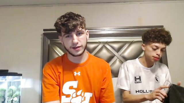 Two cute curly-haired twinks, one in orange shirt, close-up gay teen preview