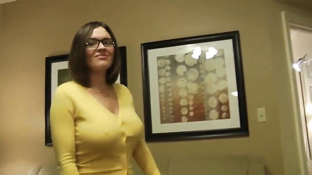 Smiling brunette MILF in tight yellow V-neck sweater showing deep cleavage