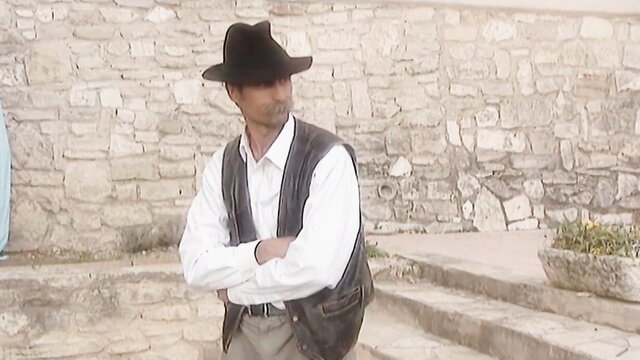 Cowboy man in vest and hat arms crossed against stone wall, Summer Wind 1997 restored