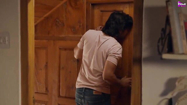 Handsome long-haired Indian man peeking through door in tight shirt and jeans