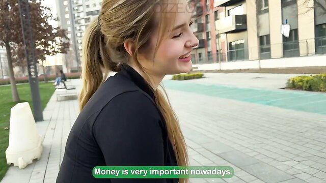 Blonde bimbo smiles outdoors in tight black top, money matters