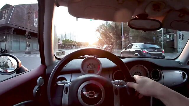 POV hand on wheel driving Mini Cooper thru crowded streets at sunset