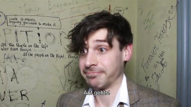 Amateur guy with messy hair smirking at camera in front of graffiti wall