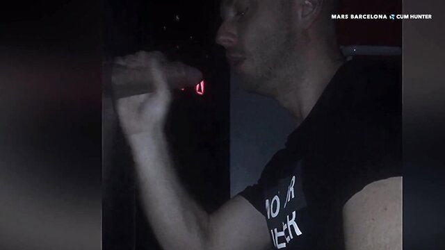 Man gripping thick cock at glory hole, red light glows