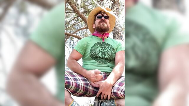 Bearded muscular man in green wolf shirt and plaid shorts bator posing outdoors