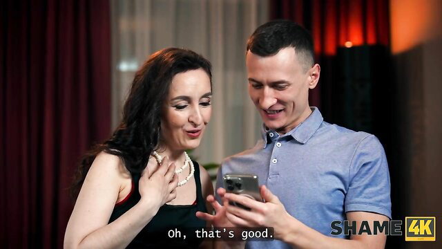 Brunette MILF and fit guy smiling at phone in erotic scene