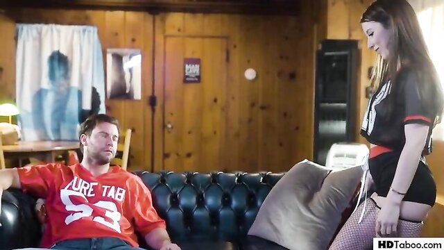 Hot brunette in fishnets stands over guy on couch in taboo scene