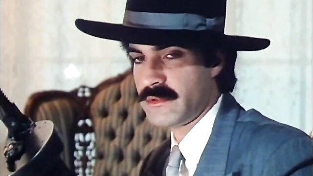Handsome mustached man in hat and suit holds vintage gun close-up