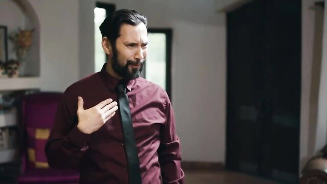 Handsome bearded man in maroon shirt and black tie poses seductively indoors