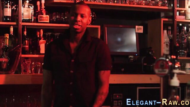 Black bartender smiling in dimly lit bar shelves background