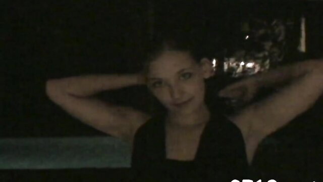 Hot brunette teen poses topless with arms up in dark bedroom