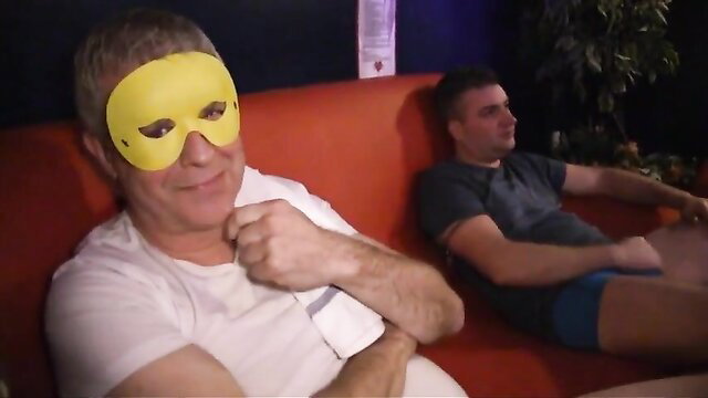 Two men in masks and underwear on couch in gangbang blonde theater scene