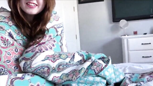 Young redhead Alana smiling in bed wrapped in colorful blanket