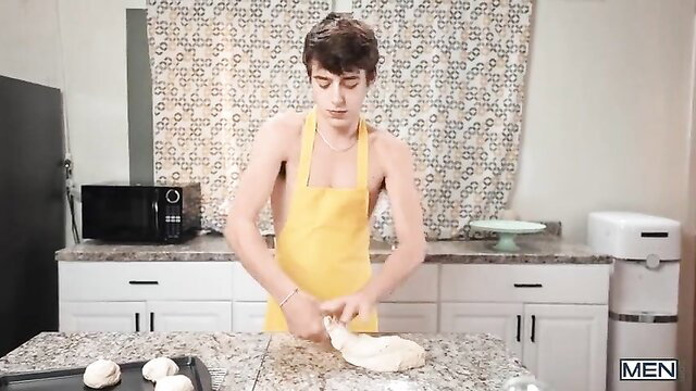 Joey Mills topless in yellow apron kneading dough in kitchen