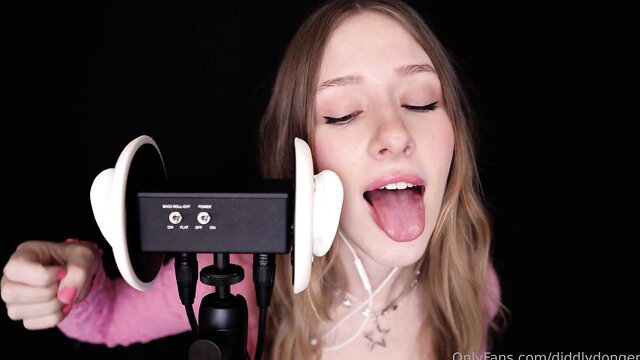 Blonde ASMR girl sticks out tongue with headphones on pink top