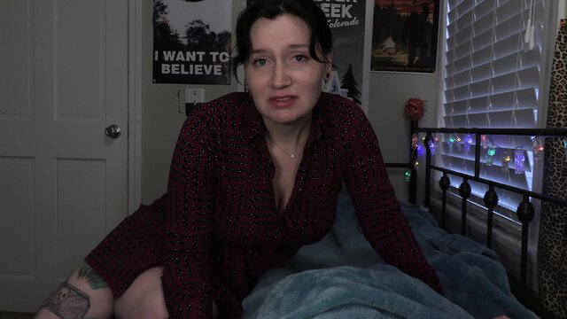 Bettie Bondage in sexy red dress on bed, teasing cleavage