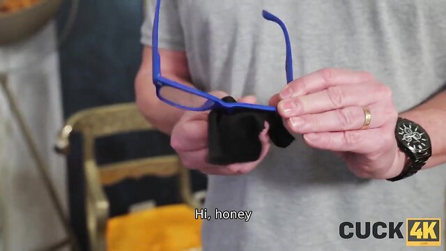 Husband greets wife holding blue glasses in cuckold tease scene