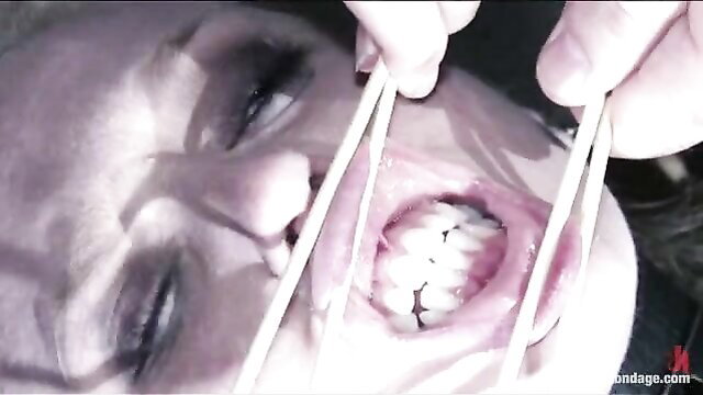 Hot slave struggles with chopsticks prying open her mouth in bondage gear