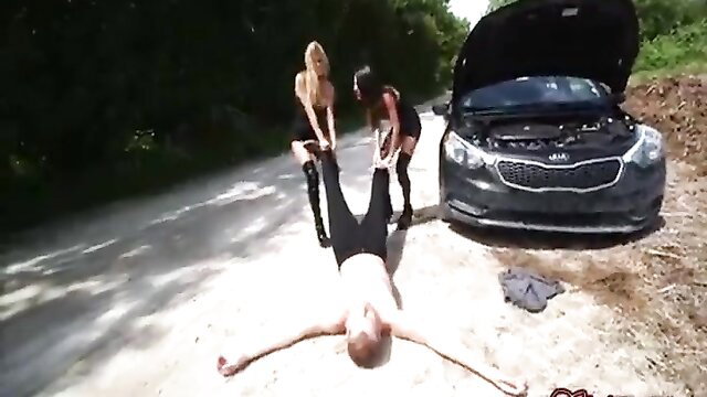 Two blonde and brunette dominatrixes in stockings trampling nude man by car
