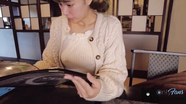 Asian woman in cardigan reading book at cafe table, OnlyFans teaser