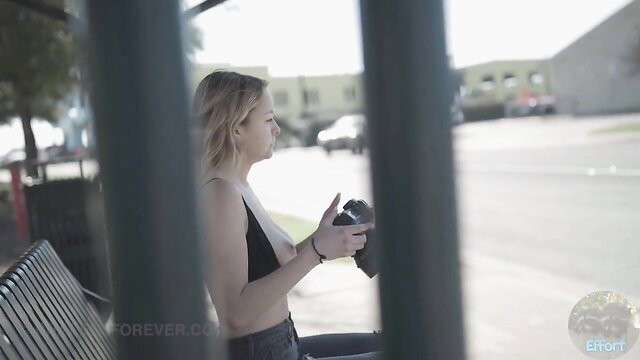 Blonde babe in black bralette holds camera at bus stop, sexy candid shot