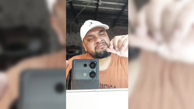Muscular Latino man in cap picks nose and poses close-up selfie
