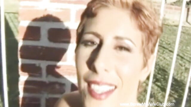 Short-haired redhead swinger behind bars smiles at shadow in sunny yard