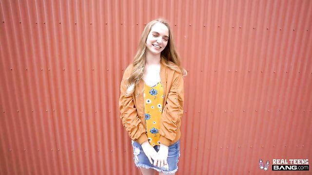 Smiling Russian teen in orange jacket and mini skirt poses sexy