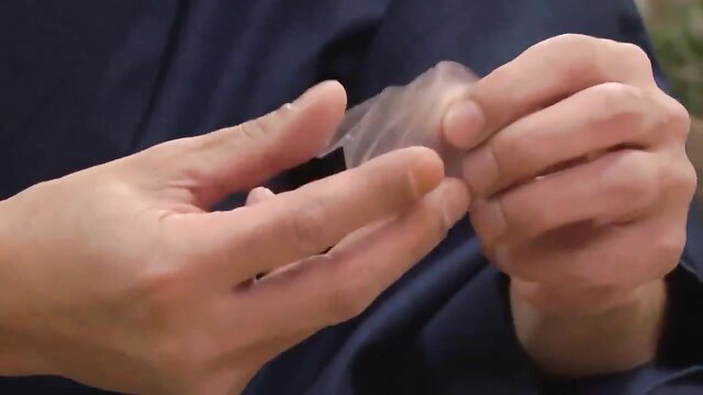 Asian man in dark robe handling condom close-up, cheating scene