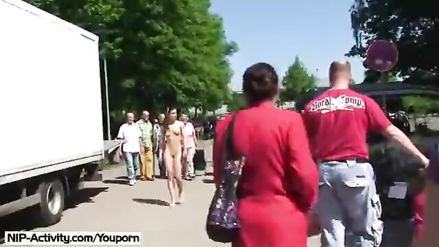 Naked brunette cutie walks nude in public street with clothed crowd