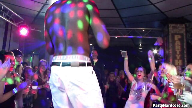 Shirtless black man in white pants dances with excited crowd at kinky party
