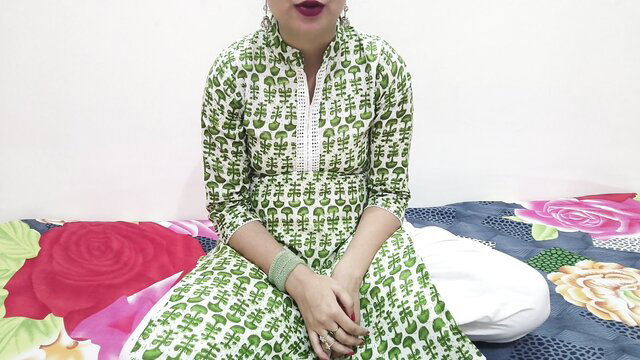 Indian beauty in green printed dress sits on bed, red lips pout seductively
